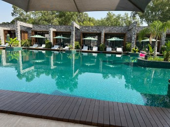 Swimming pool with wooden deck, exotic plants, umbrellas and sunbeds at luxury resort