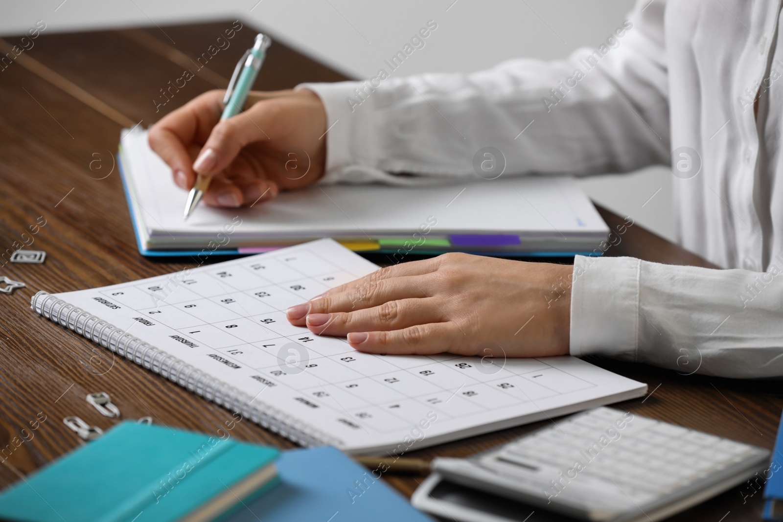 Photo of Woman making schedule using calendar at wooden table, closeup