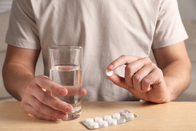 Photo of Man with glass of water and pill at wooden table, closeup