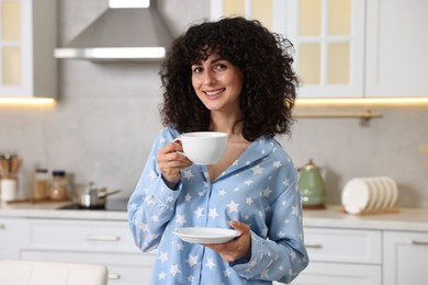 Beautiful young woman in stylish pyjama with cup of drink in kitchen