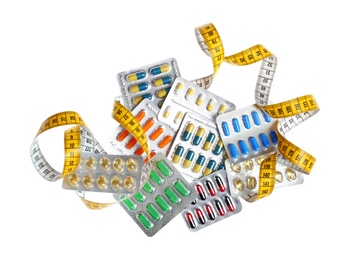 Weight loss pills in blister packs and measuring tape on white background, top view