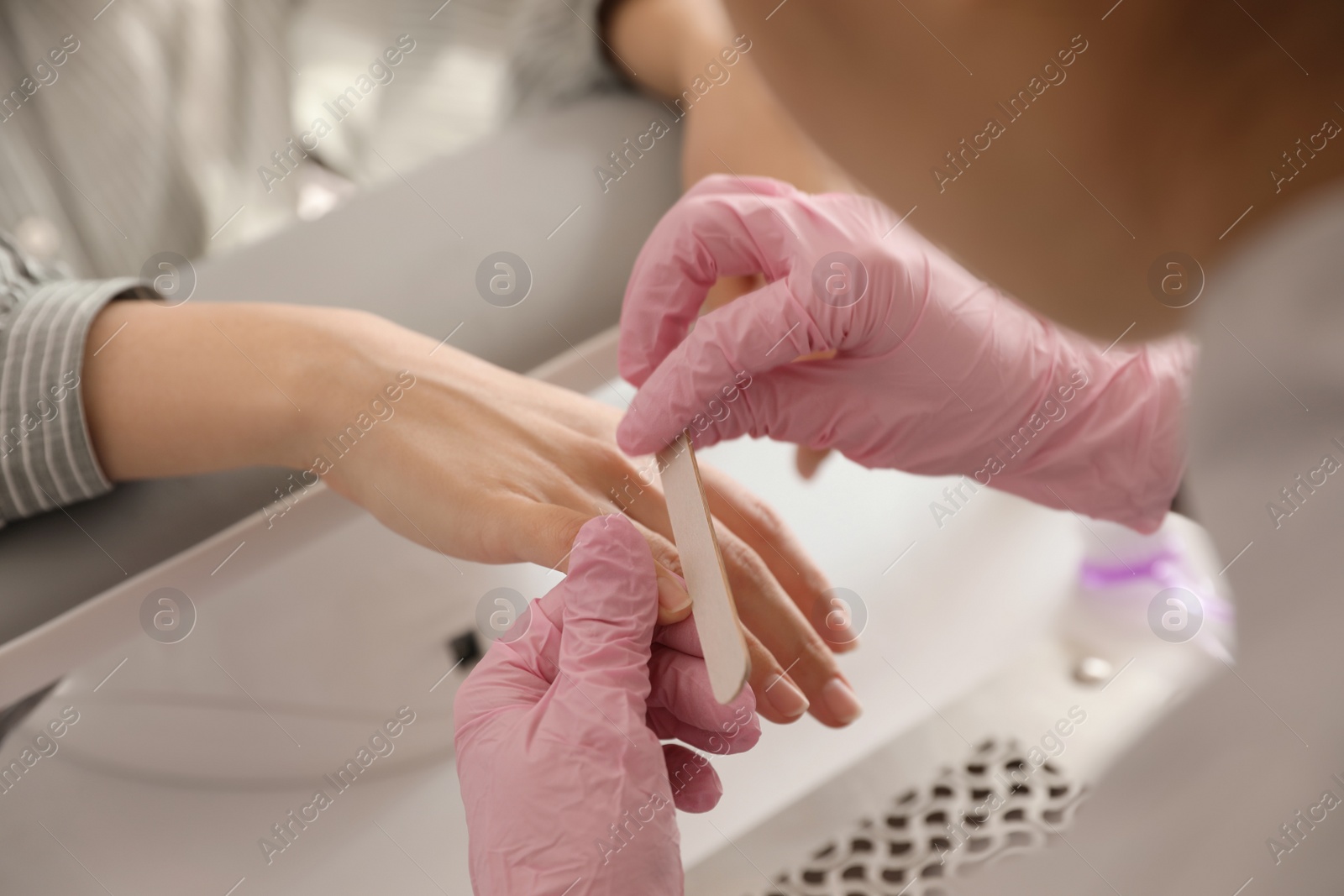 Photo of Professional manicurist filing client's nails in beauty salon, closeup