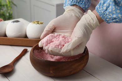 Photo of Woman in gloves making bath bomb mixture at white table indoors, closeup