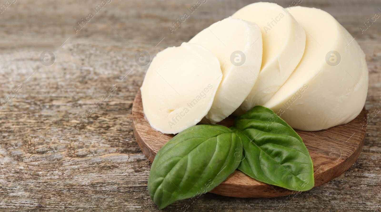 Photo of Board with tasty mozzarella slices and basil leaves on wooden table, closeup. Space for text