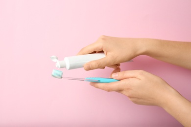 Woman squeezing toothpaste on brush against color background