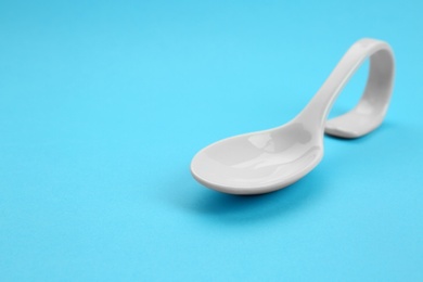 Photo of Clean empty ceramic appetizer spoon on blue background, space for text