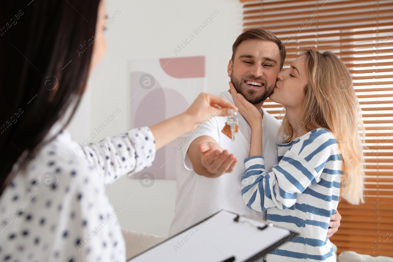 Photo of Real estate agent giving key to happy young couple in new house