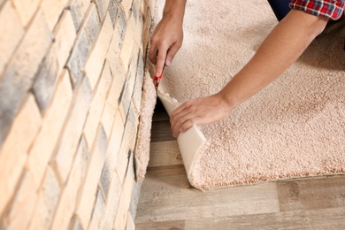 Man cutting new carpet flooring indoors, closeup. Space for text