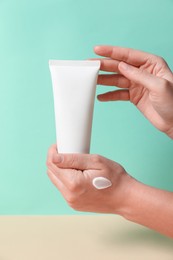 Photo of Tube of hand cream on beige table against turquoise background, closeup