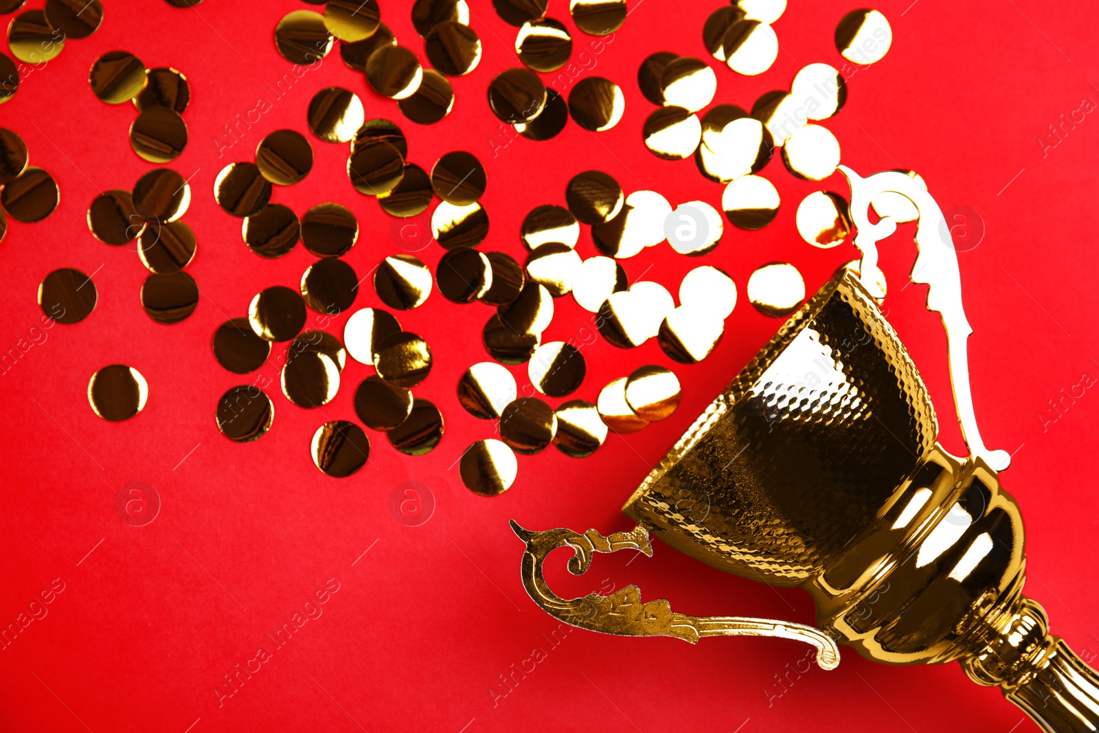Photo of Gold trophy cup and confetti on red background, flat lay. Space for text