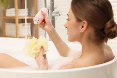 Woman pouring shower gel onto mesh pouf in bath indoors