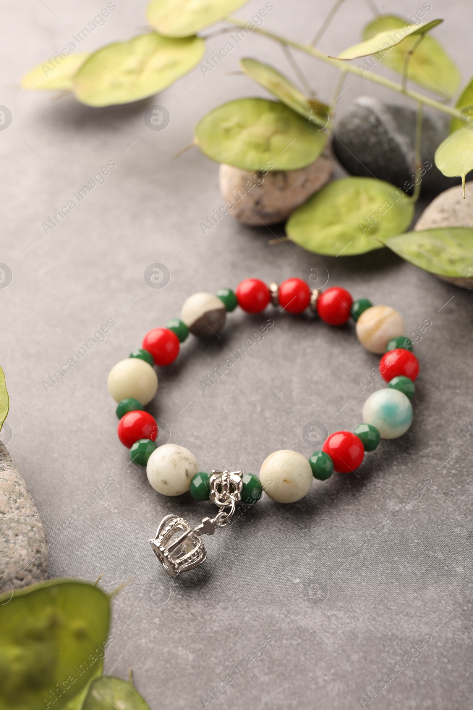 Photo of Beautiful bracelet with gemstones, leaves and stones on grey background