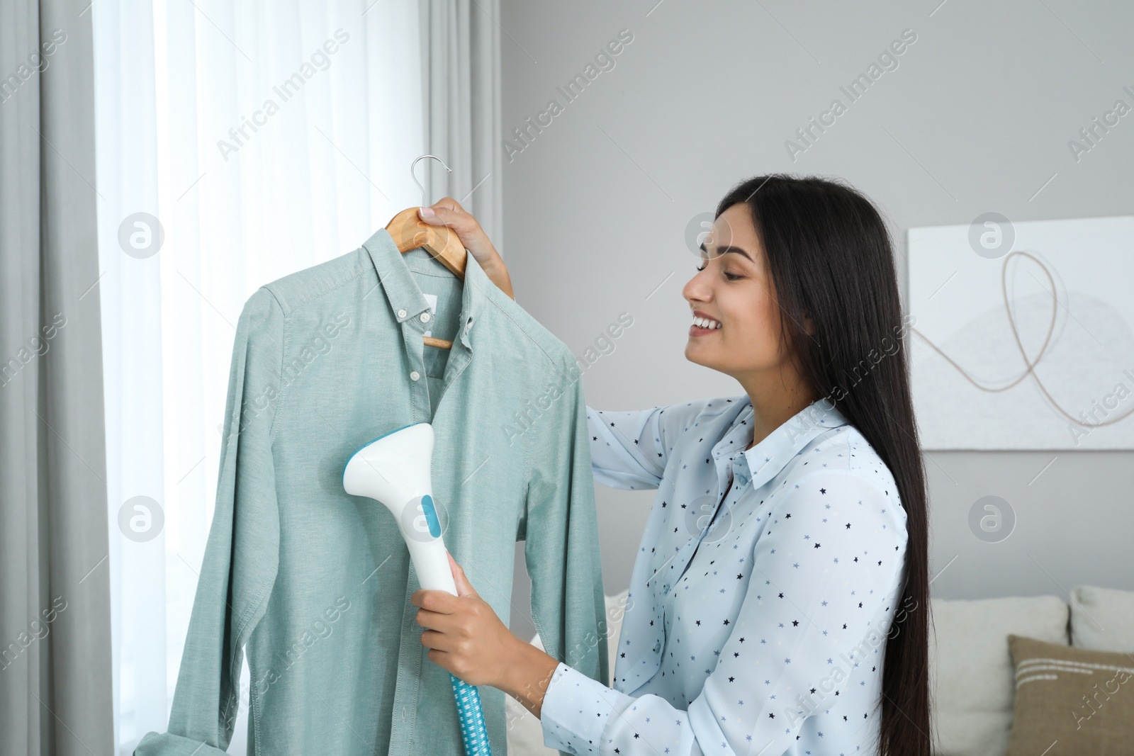 Photo of Woman steaming shirt on hanger at home