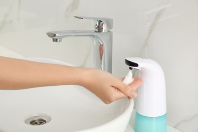 Woman using automatic soap dispenser in bathroom, closeup