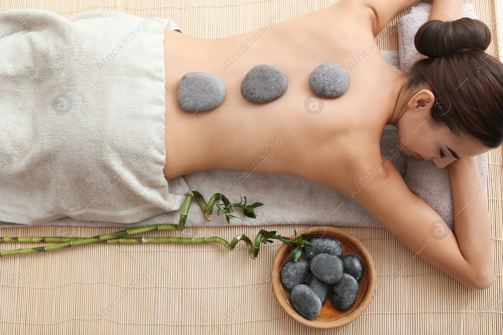 Photo of Beautiful young woman getting hot stone massage in spa salon, top view