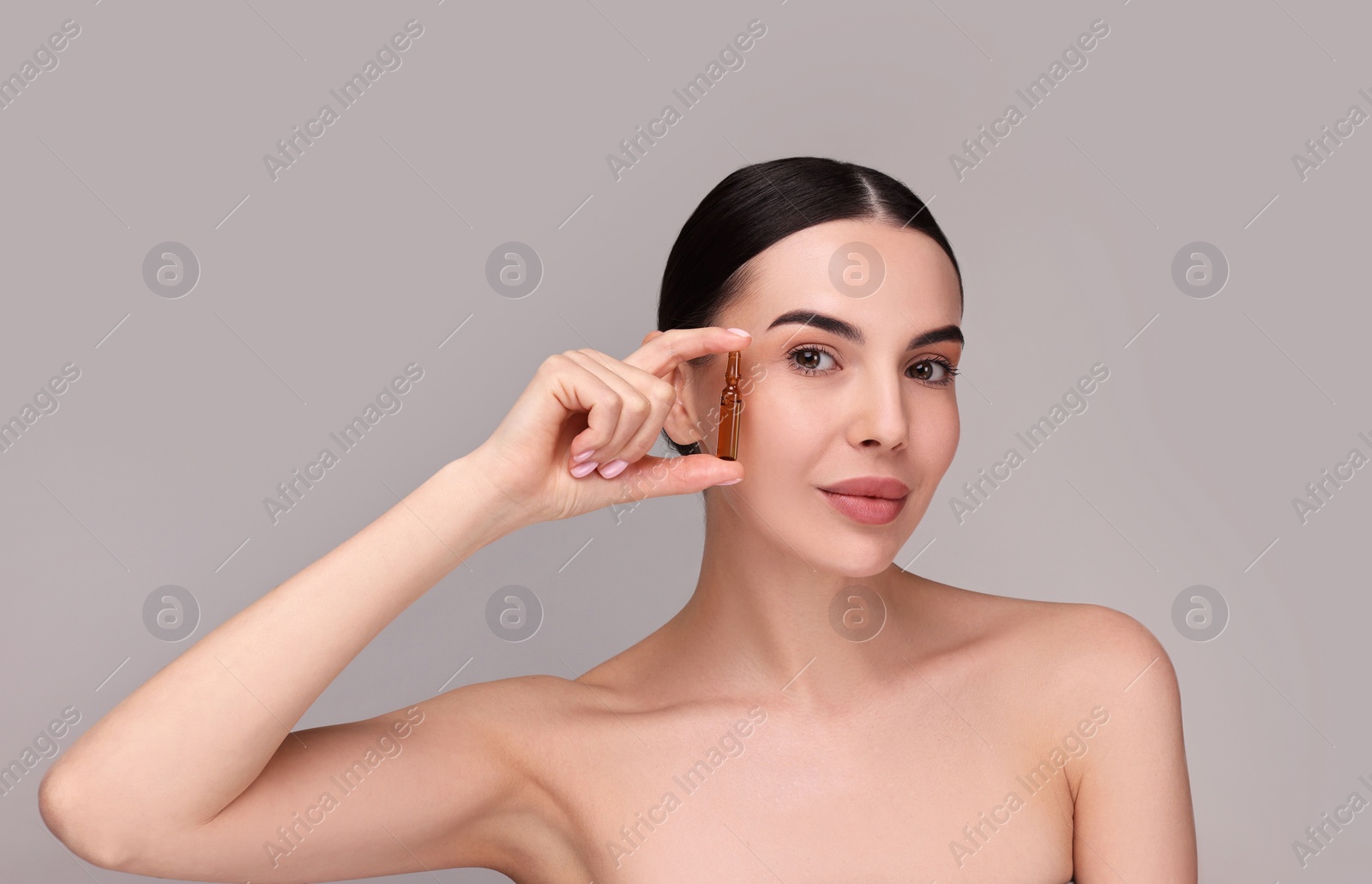 Photo of Beautiful young woman holding skincare ampoule on grey background