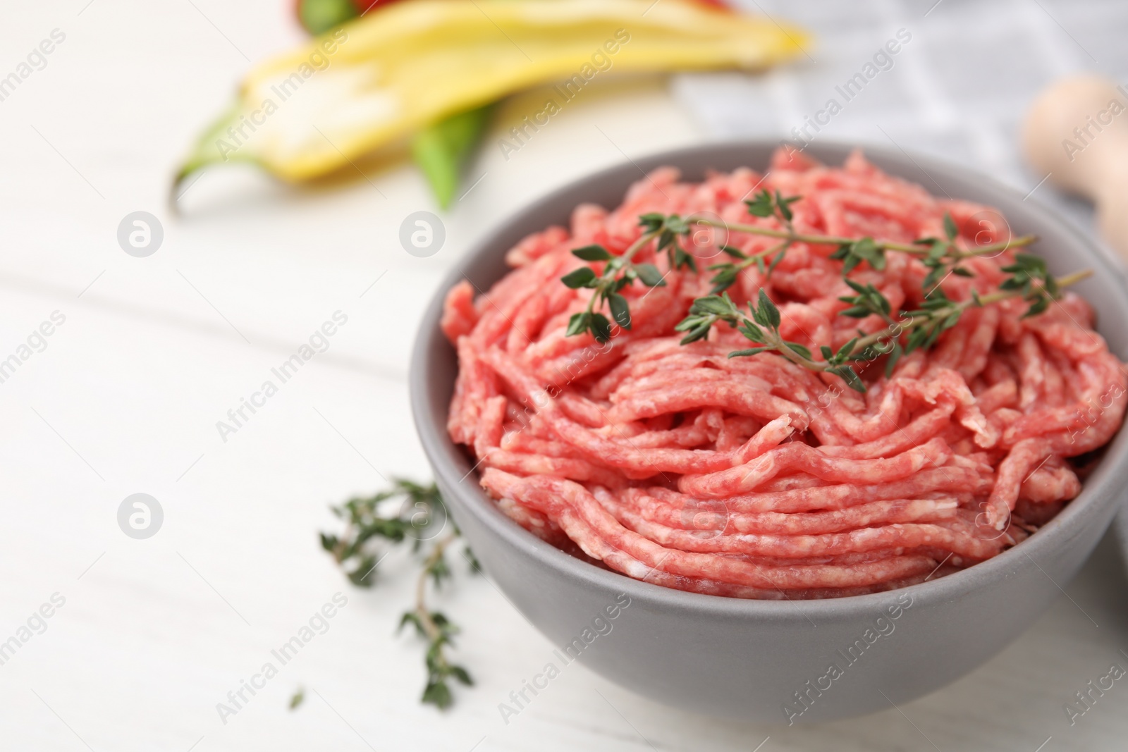 Photo of Fresh raw ground meat and thyme in bowl on white table, closeup. Space for text