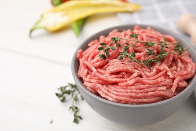 Photo of Fresh raw ground meat and thyme in bowl on white table, closeup. Space for text