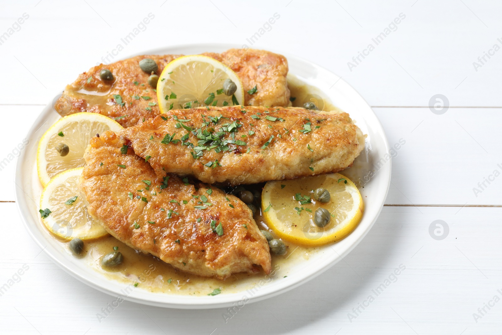 Photo of Delicious chicken piccata on white wooden table, closeup