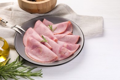 Photo of Tasty ham with rosemary and carving fork on white wooden table, space for text