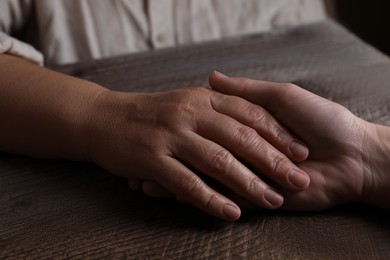 Woman holding hands with her mother at wooden table, closeup