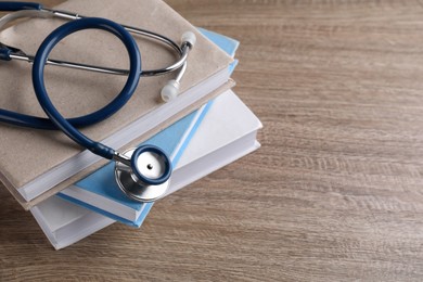 Photo of Student textbooks and stethoscope on wooden table, closeup view with space for text Medical education