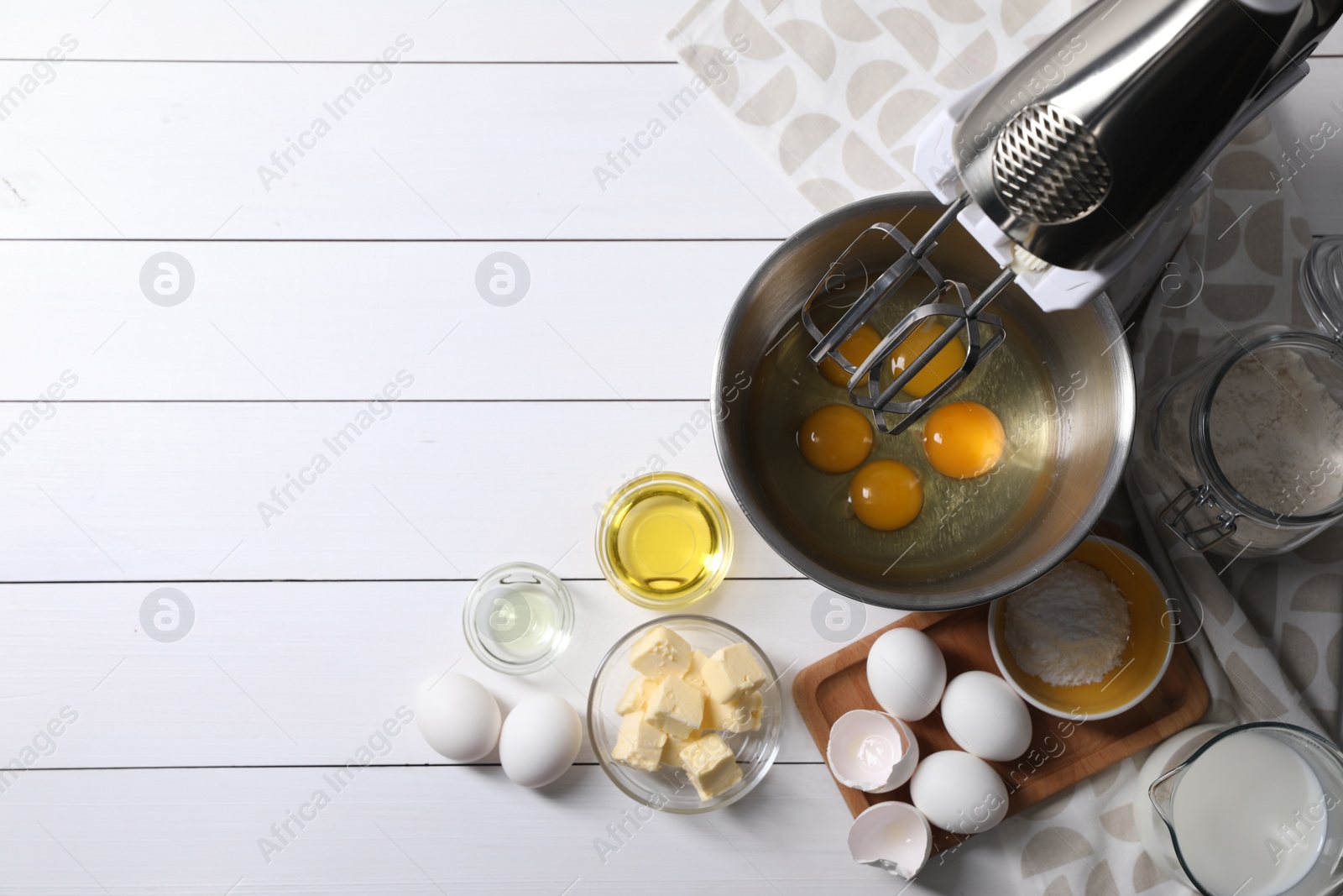 Photo of Making dough. Raw eggs in bowl of stand mixer and ingredients on white wooden table, flat lay with space for text