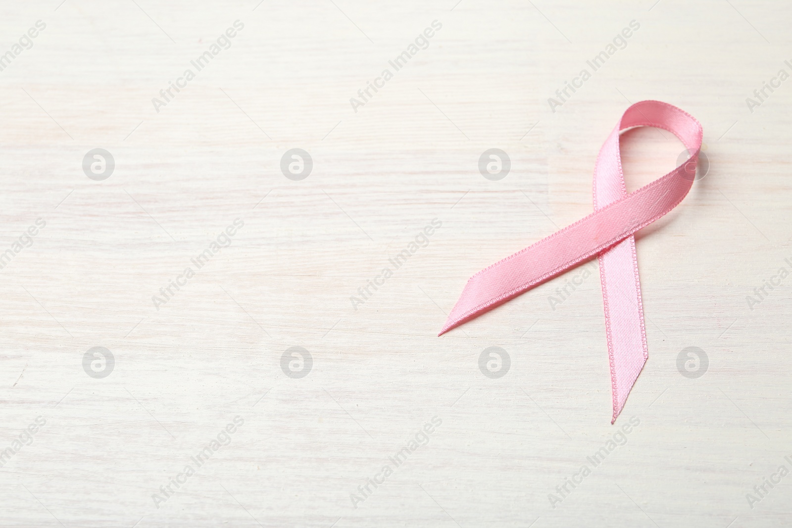 Photo of Pink awareness ribbon on light wooden table, above view. Space for text