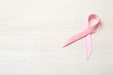 Pink awareness ribbon on light wooden table, above view. Space for text