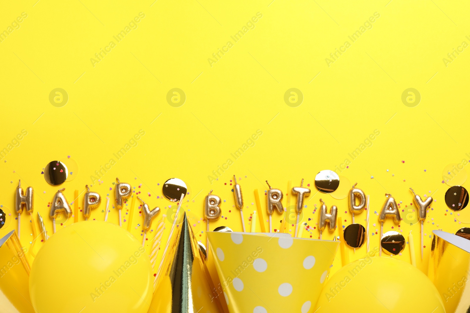 Photo of Phrase Happy Birthday of candles and party decor on yellow background, flat lay. Space for text