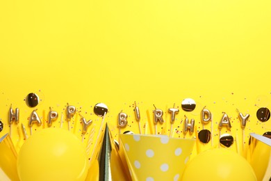 Phrase Happy Birthday of candles and party decor on yellow background, flat lay. Space for text