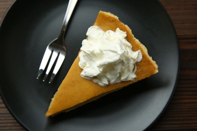 Piece of delicious pumpkin pie with whipped cream and fork on wooden table, top view