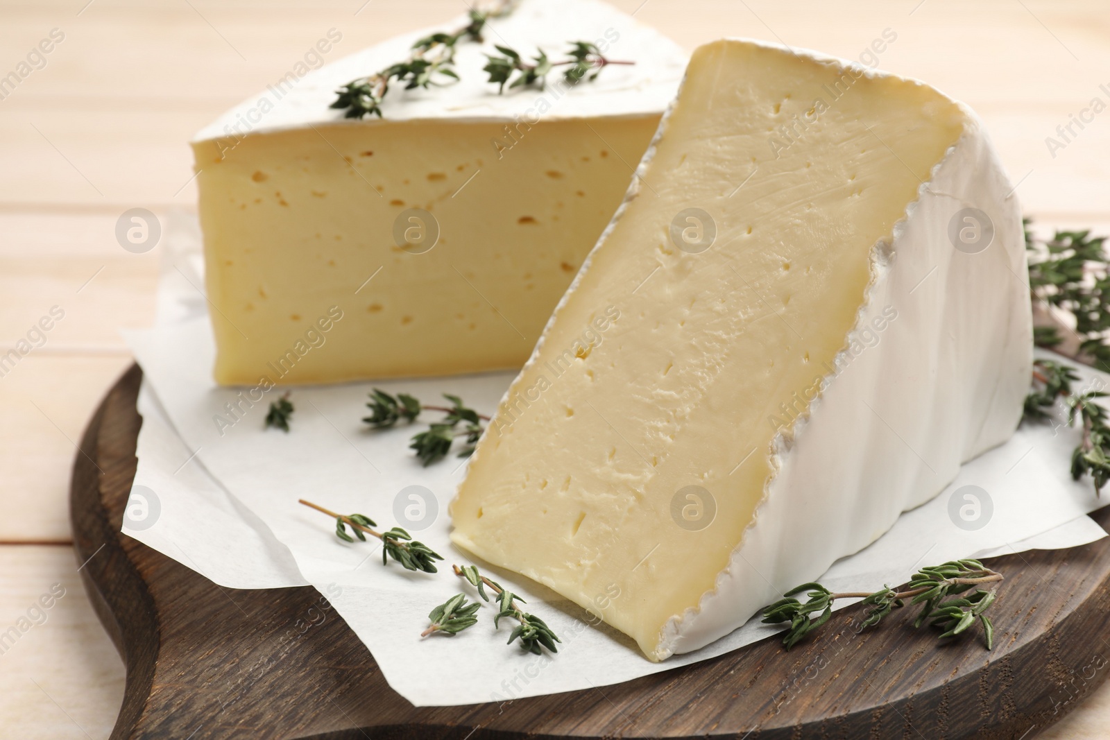 Photo of Board with pieces of tasty camembert cheese and thyme on light wooden table, closeup