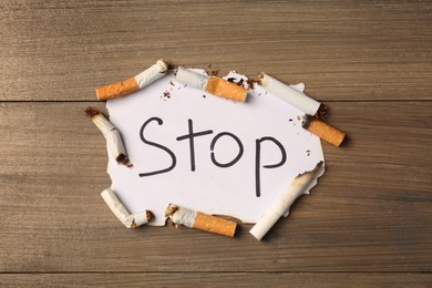 Burnt cigarettes and word Stop written on paper on wooden table, flat lay. No smoking concept