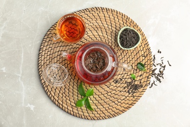 Teapot with hot aromatic tea, dry and fresh leaves on wicker mat, top view