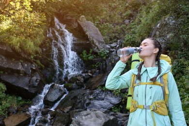 Tourist drinking water near waterfall in mountains. Space for text