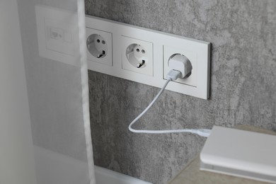 Power bank plugged into electric socket on grey wall