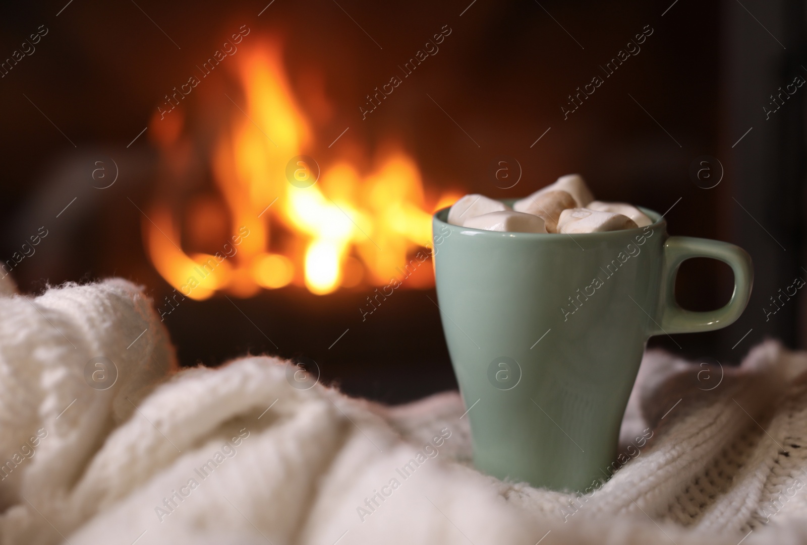 Photo of Delicious sweet cocoa with marshmallows and blurred fireplace on background