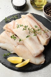 Photo of Pieces of raw cod fish, lemon and spices on light grey table