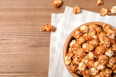 Photo of Bowl with caramel popcorn on wooden background, top view. Space for text