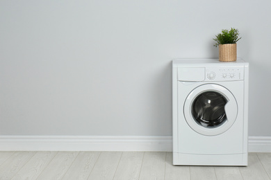 Modern washing machine with houseplant near white wall, space for text. Laundry day