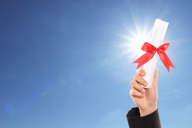 Graduated student holding diploma against blue sky on sunny day, closeup