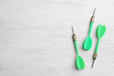 Green dart arrows on white wooden table, flat lay with space for text