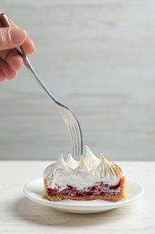 Photo of Woman eating delicious tartlet dessert with meringue and jam at white table, closeup