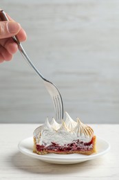 Woman eating delicious tartlet dessert with meringue and jam at white table, closeup