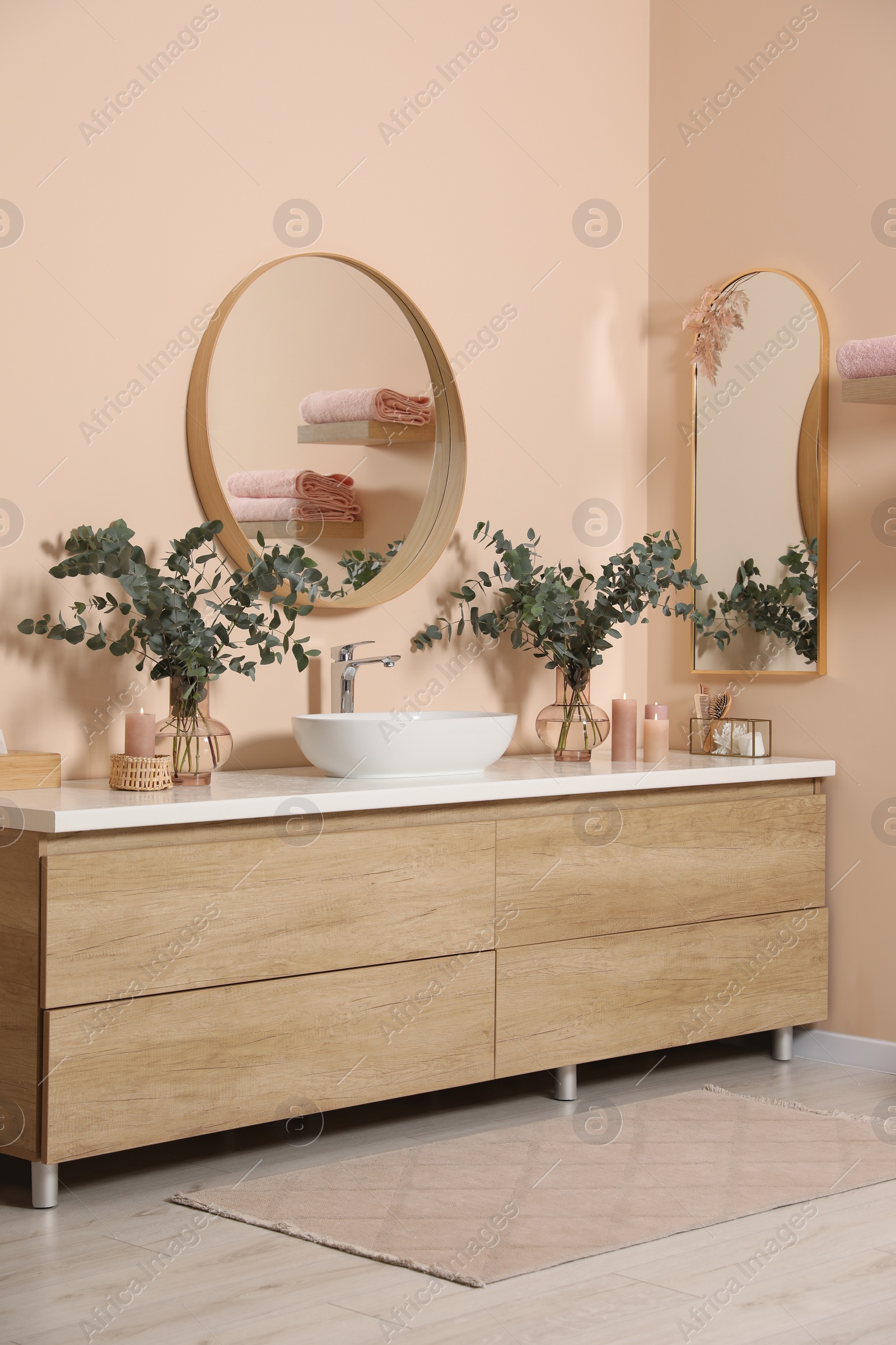 Photo of Modern bathroom interior with stylish mirror, eucalyptus branches, vessel sink and wooden vanity