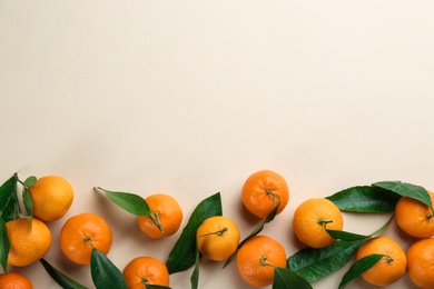 Photo of Fresh ripe tangerines with green leaves on beige background, flat lay. Space for text