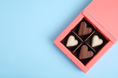 Photo of Tasty heart shaped chocolate candies on light blue background, top view with space for text. Happy Valentine's day