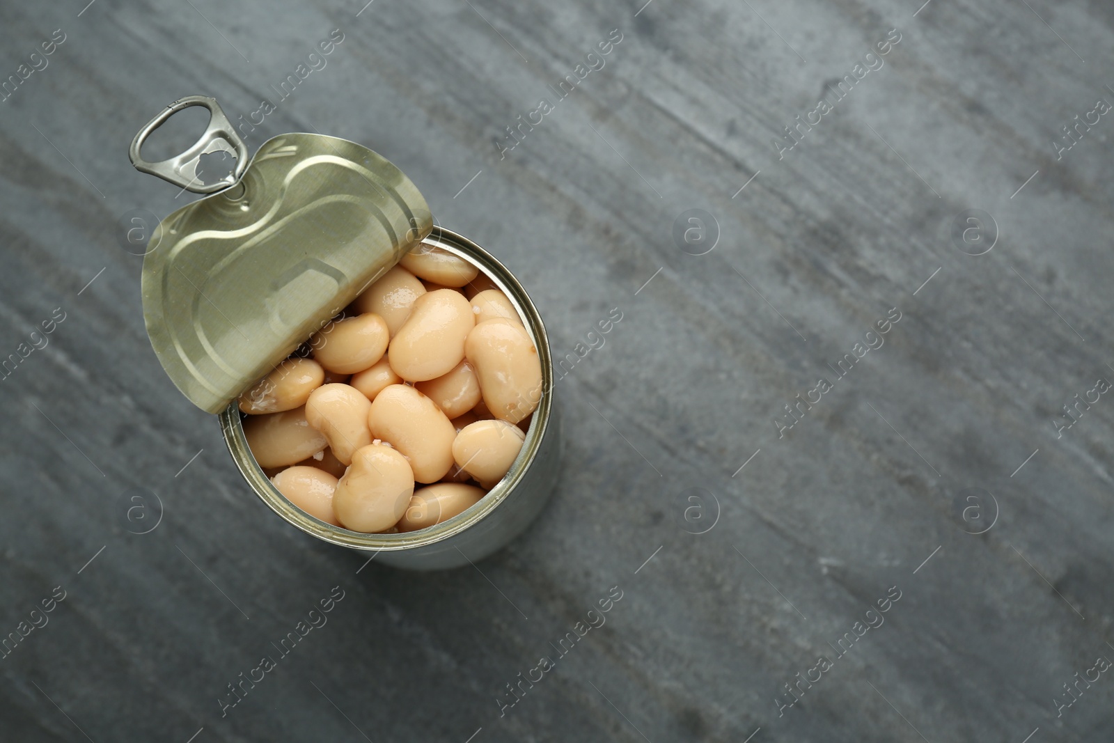 Photo of Tin can of canned white kidney beans on grey table, top view. Space for text