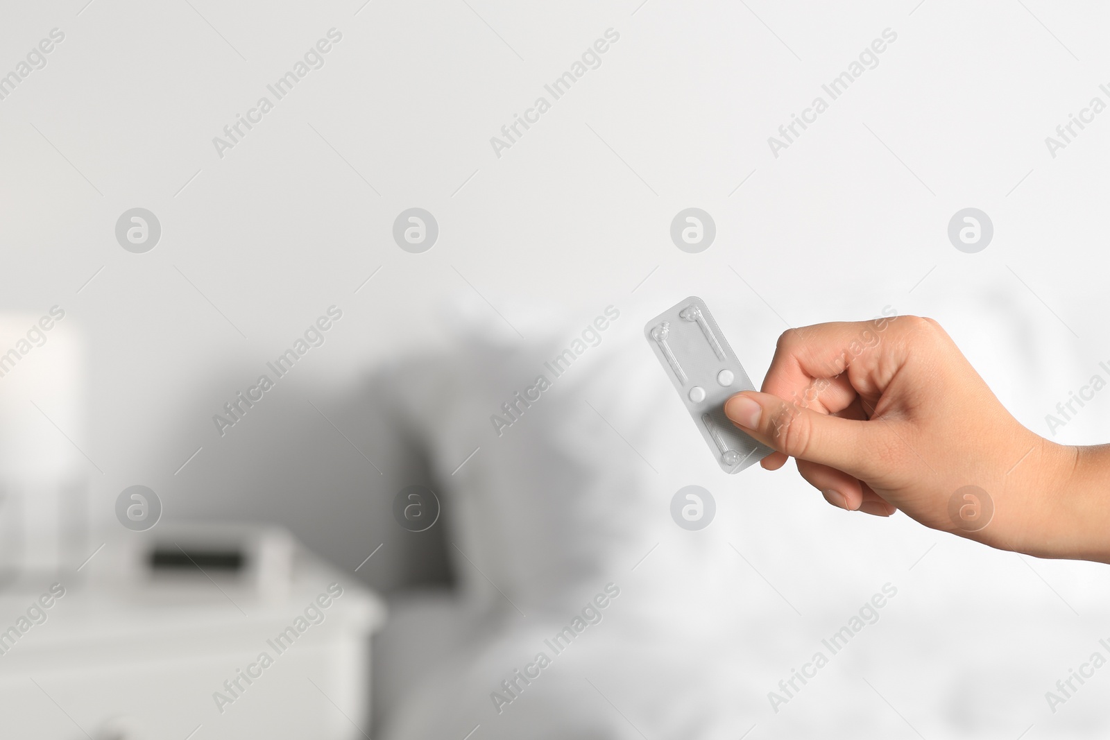 Photo of Woman holding blister of emergency contraception pills against blurred background, closeup. Space for text